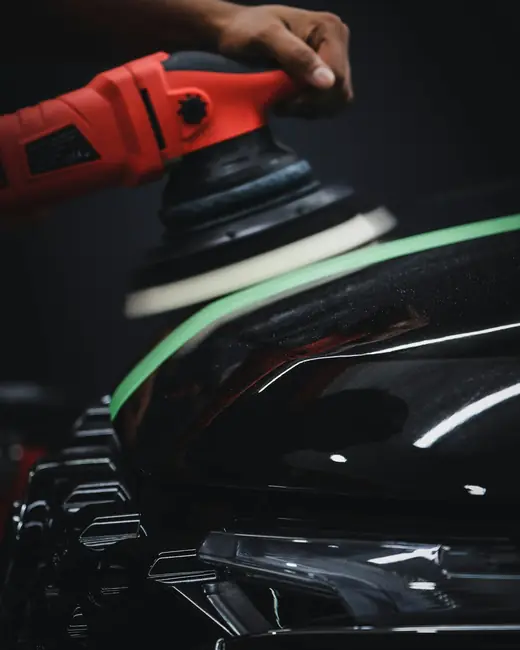 Detailer machine-polishing the hood of a black car