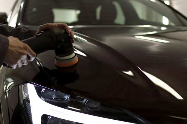 Hands guiding a dual-action polisher across dark paint