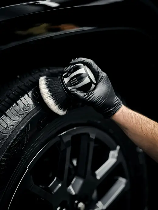 Gloved hand cleaning a tire sidewall with a soft brush