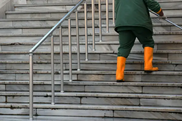 Worker in rubber boots washing outdoor stone steps