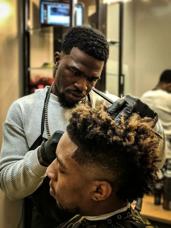 Barber shaping curly hair on top with a fade on the sides
