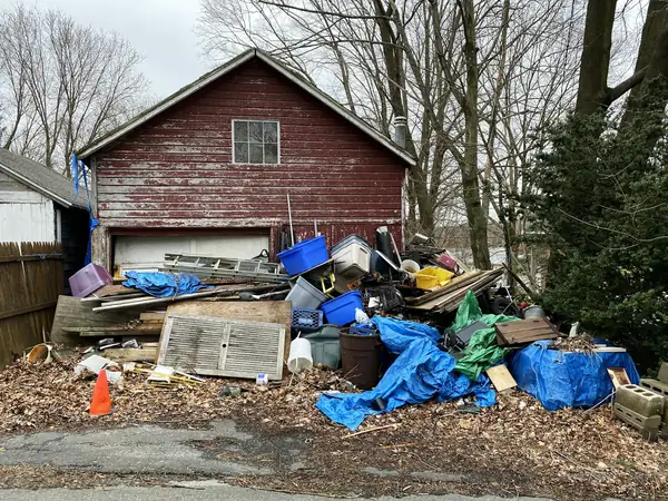 Large pile of junk, tarps and boards in front of an old barn garage