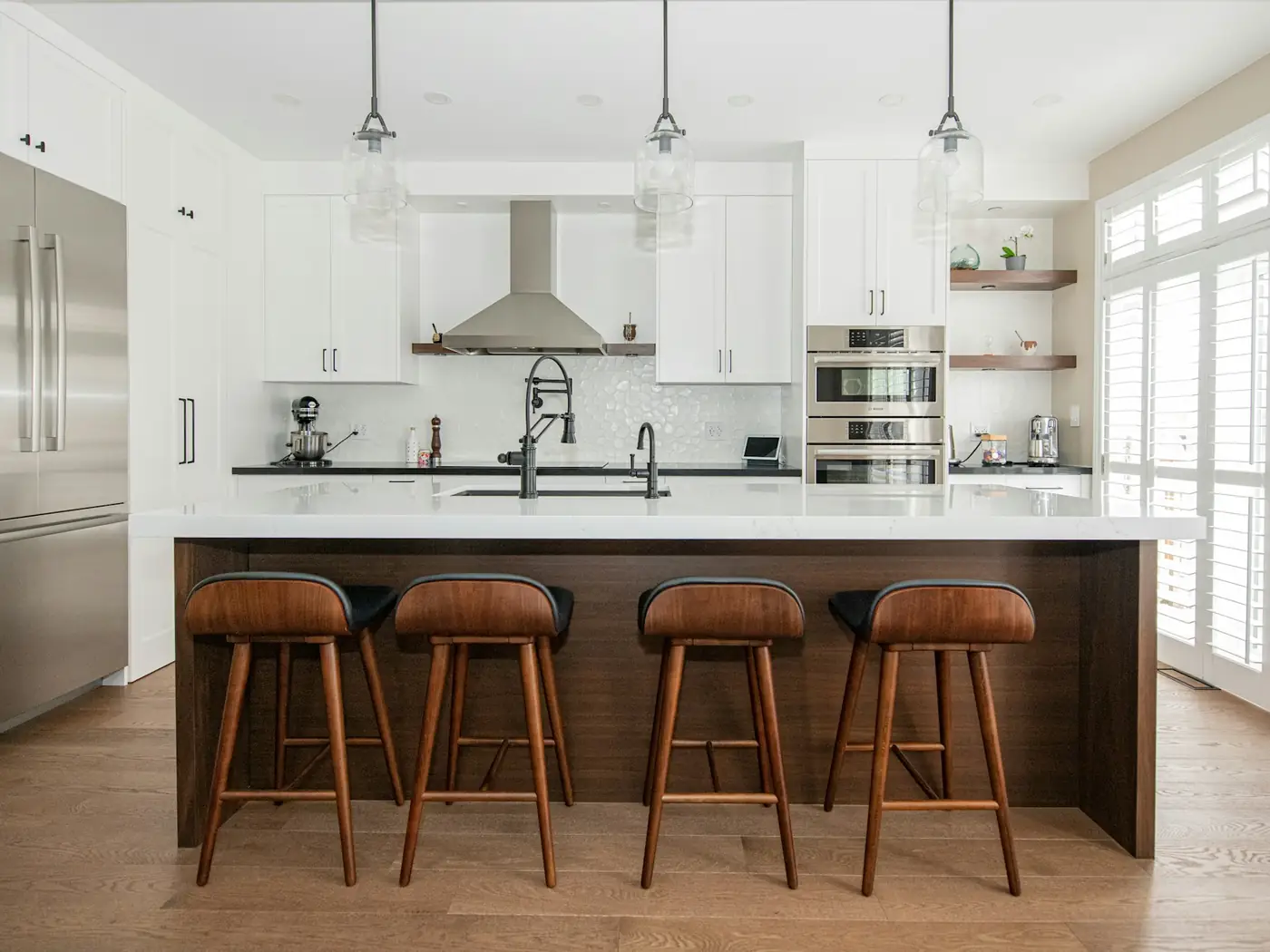 Bright modern kitchen with white cabinets, walnut island and leather stools