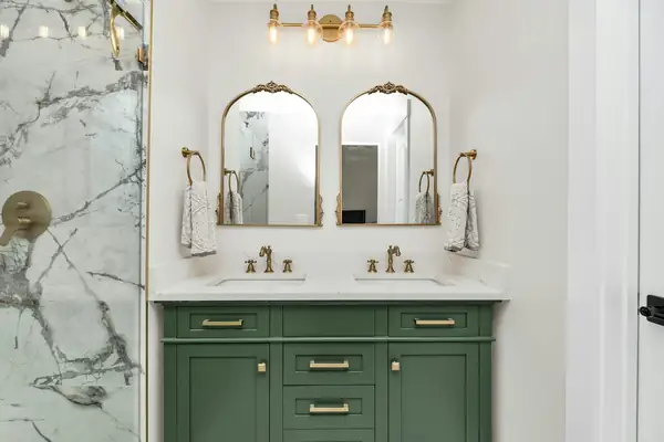 Bathroom with a green double vanity, brass fixtures and arched mirrors