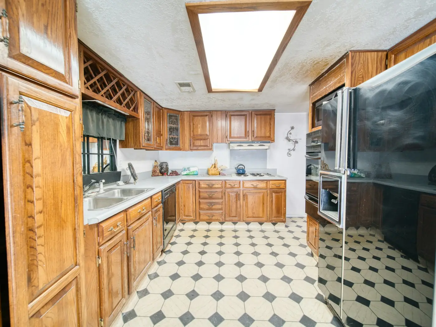 Dated kitchen with orange oak cabinets, a fluorescent light box and checkered vinyl floor